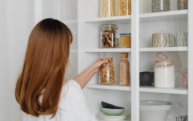 Woman organizing your new pantry by arranging jars of pasta, grains, and dried fruits on white shelves