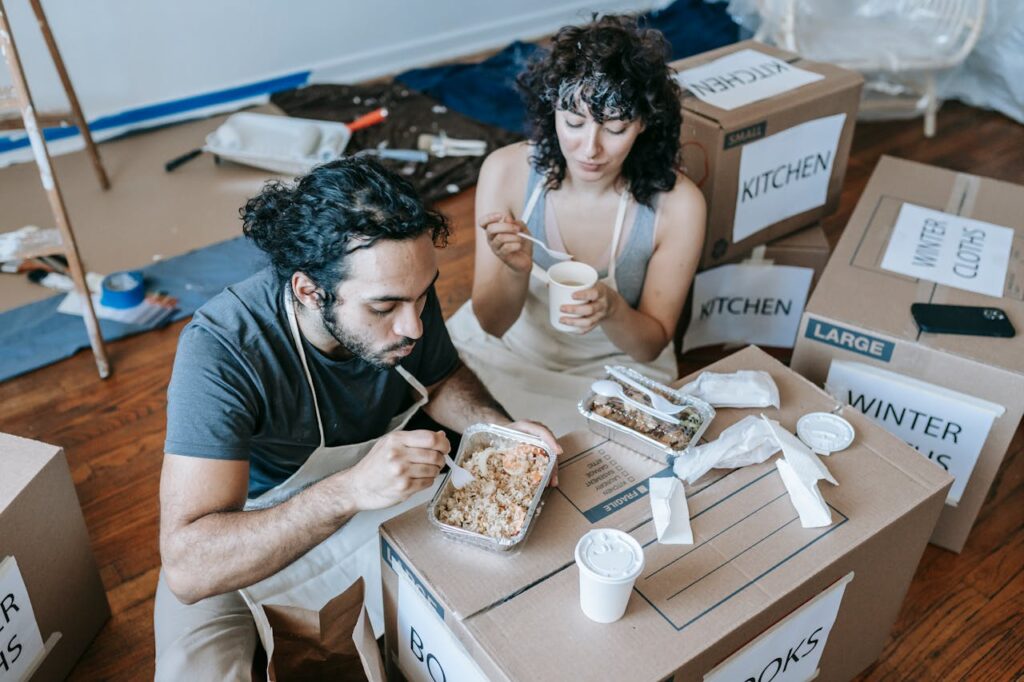 Couple eating on cardboard moving boxes.